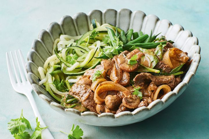 A bowl of beef stroganoff served with green beans and zucchini noodles.